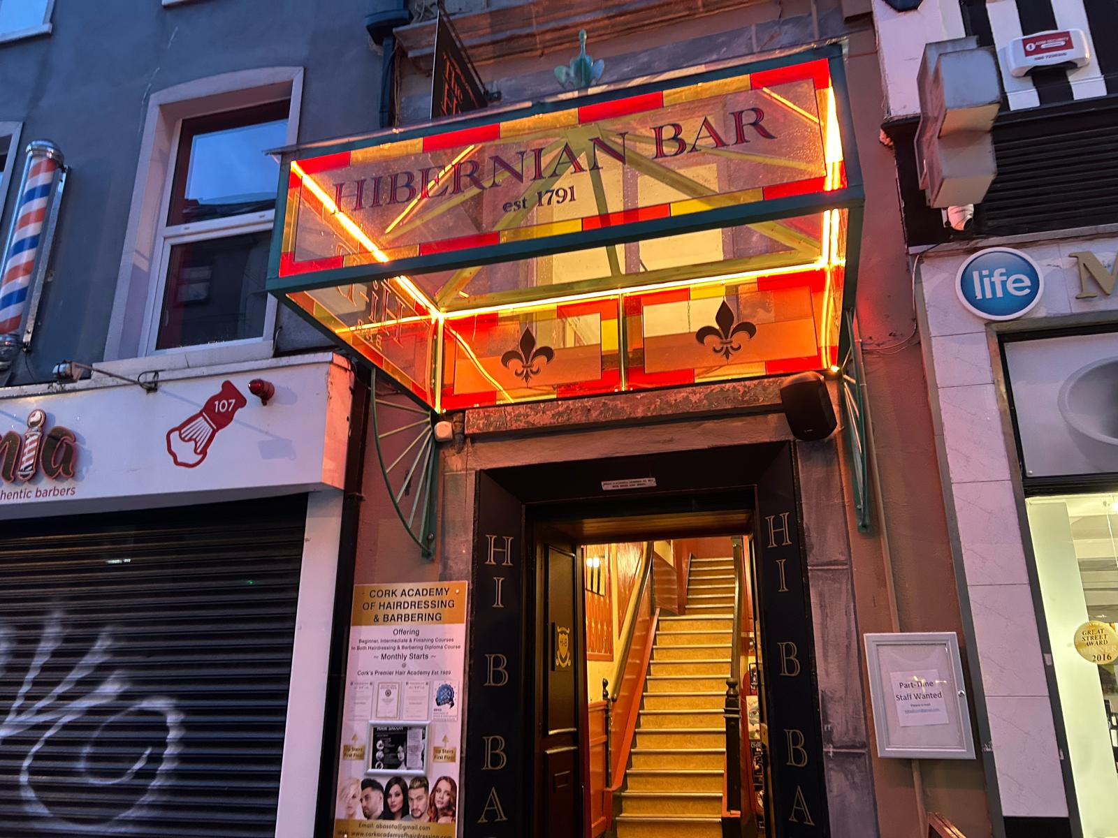 Illuminated Hibernian Bar entrance sign above the doorway to the Hi-B Bar in Cork city at dusk.